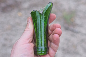 the hand of an aggressive criminal holds a piece of glass green sharp broken bottle on the street
