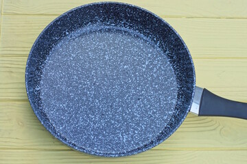 one large open frying pan with a gray granite surface and a black handle stands on a yellow table