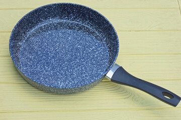 one large open frying pan with a gray granite surface and a black handle stands on a yellow table