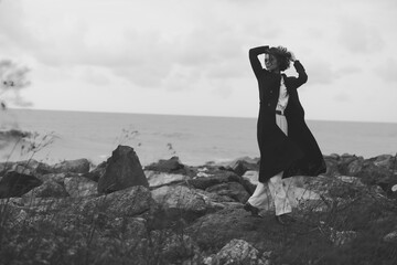 Couple, wind, coats, shore, landscape, black, white, sea, motion, fashion, outdoor scene with two figures embracing among rocky terrain along a windy coastline, capturing raw energy and timeless