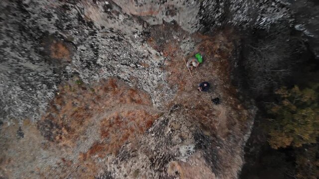 aerial view hikers near ancient fortress on rugged mountain cliffs during guided hike, drone frames tiny figures on textured rock and weathered stone walls, dramatic shadows and sweeping valley