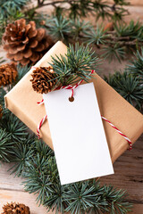 Christmas rectangle gift tag mockup with present box, product label mockup, with natural fir tree branch, cones and Christmas decoration, Christmas sale concept. Blank paper rectangular name tag