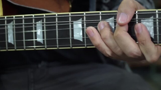 Close-up of a musician's hand playing a chord on an electric guitar neck with trapezoid inlays.
