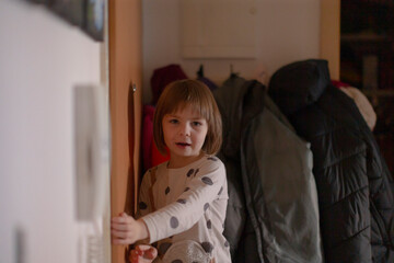 Girl checks doorway happily smiling, Young child inspects corridor with cheerful curiosity, Youthful girl carefully looks into entrance with happy and eager expression early in day