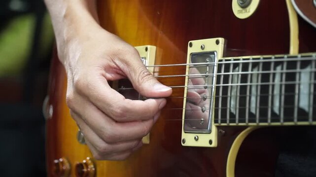Close-up of a musician's hand playing an electric guitar with humbucker pickups.