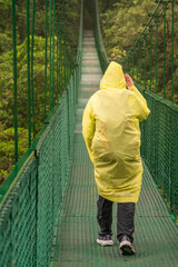 Obraz premium Rain soaked tourist crossing the moss and tree filled valley on hanging bridge in rainforest of Monteverde in Costa Rica