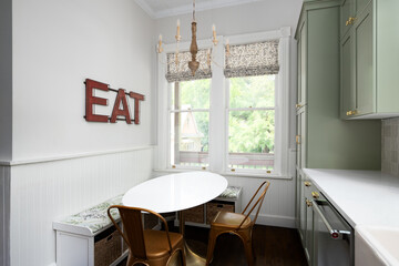 A dining room in a kitchen with sage green cabinets and white countertop. A table, bronze chairs,...