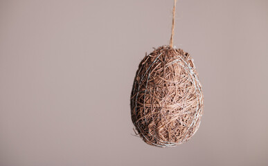 Natural straw Easter egg hanging on neutral background