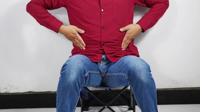 Stomach ache, stomach cramps and a man sitting in a chair at work due to indigestion, diarrhea, or food poisoning. A man has a stomach ache due to constipation, IBS, or abdominal muscle tension at hom