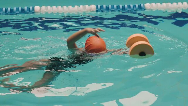 Child learning to swim in indoor pool using foam dumbbells, kids swimming lesson with flotation equipment, healthy sport activity and early water training concept