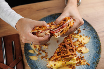 Enjoying a savory waffle sandwich filled with meat and cheese for lunch at a casual dining spot