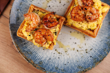 Shrimp and scrambled eggs served on crispy waffles with herbs and seasoning on a decorative plate