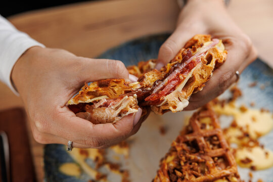 Delicious food preparation showing hands pulling apart a sandwich made with unique ingredients at a cozy dining location