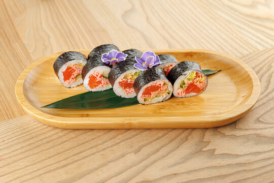 Savory sushi rolls served on a wooden plate with decorative flowers and leaves in a light setting