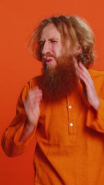 I cant hear you. What. Caucasian man trying hear you looking confused and frowning keeping arm near ear for louder voice asking to repeat, to hear information, deafness. Young guy on orange background