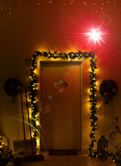 A White Front Door Is Framed By Glowing Holiday Garlands And Wreaths Under A Radiant Red Moravian Star At Night