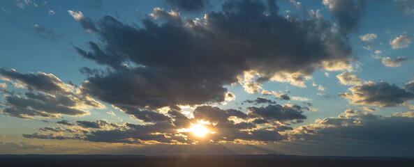 Dramatic sunset sky with sun rays breaking through dark storm clouds over a distant horizon, creating a moody golden-hour cloudscape background with copy space.