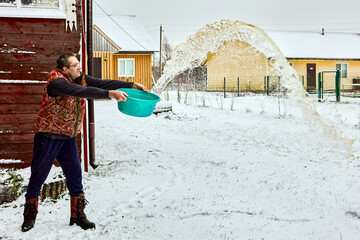 Spilling dirty water on snow in yard after wet cleaning inside, mature man spills washbasin with sharp motion, water forms arc.