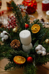 A cozy Christmas wreath with pine branches, white candles, dried oranges, cotton and red ornaments.