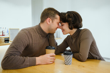 Couple shares a warm, romantic moment at a cafe, leaning foreheads together and enjoying coffee