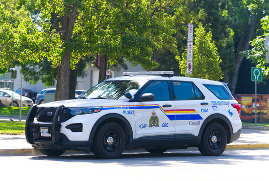 Ford Explorer RCMP police vehicle law enforcement cop SUV parked at the side of a tree-lined street on a sunny warm day.