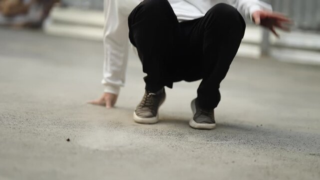 Dynamic street dance footwork on dusty concrete, close-up of agile legs and sneakers in an urban performance with energetic crouch, cross-steps, and motion in an outdoor setting