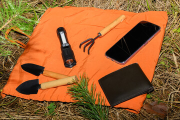 flashlight garden tools wallet and smartphone on orange fabric on the forest floor