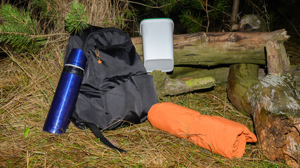 black backpack blue thermos and orange mat lying on the grass near a fallen tree