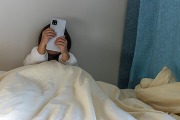 うす暗い部屋で座ってスマートフォンを見る女の子のイメージ（5歳、日本人、顔無し）