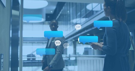 Texting business pair wearing business attire in atrium with smartphone, briefcase, chat bubbles