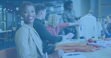 Smiling woman in beige blazer taking notes at meeting table with garment rack, copy space