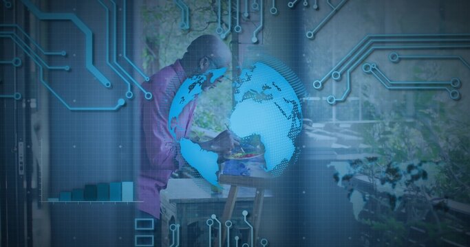 Leaning senior man wearing pink shirt writing at table at home, with holographic globe overlay - Powered by Adobe