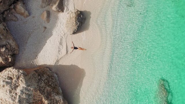 Relaxed woman sunbathing alone on quiet turquoise beach on a summer morning