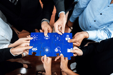 A diverse group of professionals cooperatively assembling puzzle pieces showcasing technology and security icons, symbolizing teamwork and innovation in a modern office setting. Amity