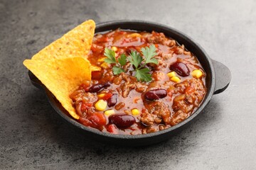 Delicious chili con carne with nachos on grey table, closeup