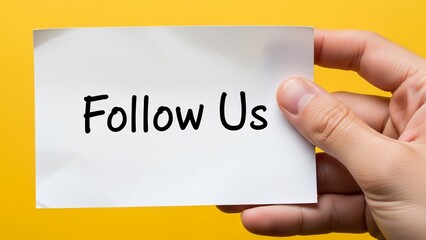 Hand holding a white card with Follow Us written on it against a yellow background