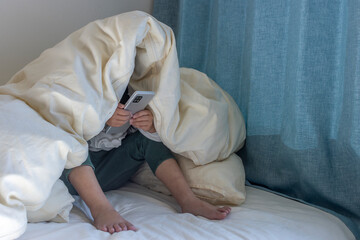うす暗い部屋で布団をかぶってスマートフォンを見る女の子のイメージ（5歳、日本人、顔無し）