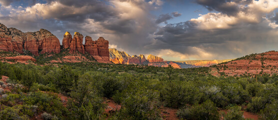 Panoramic landscape of Sedona red rocks under dramatic stormy sky with sunlit peaks, Arizona