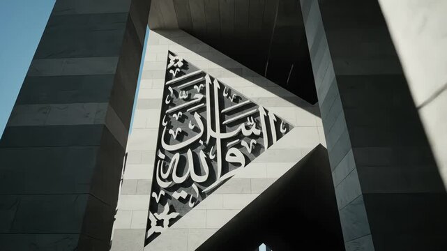 Sunlight reveals intricate Arabic calligraphy on a modern, minimalist marble building, panning up from shadow to light