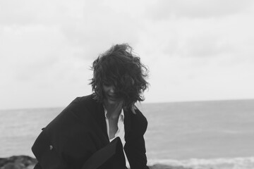 Woman on a windy coast wearing a dark jacket near the sea, monochrome photo with moody atmosphere, motion and horizon line, casual style on a dramatic shore