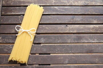 Raw pasta on wooden background and tied with a cord. Uncooked spaghetti on a wood background with a space to write. Pasta and food nutrition. Noodles recipes and cooking spaghetti.