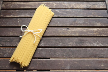 Raw pasta on wooden background and tied with a cord. Uncooked spaghetti on a wood background with a space to write. Pasta and food nutrition. Noodles recipes and cooking spaghetti.