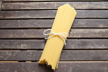 Raw pasta on wooden background and tied with a cord. Uncooked spaghetti on a wood background. Pasta and food nutrition. Noodles recipes and cooking spaghetti.