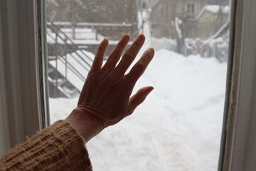 An hand of an old woman in a window with a view of snow. Woman hand on an interior window. Elder person and solitude. Old age among the elderly. 