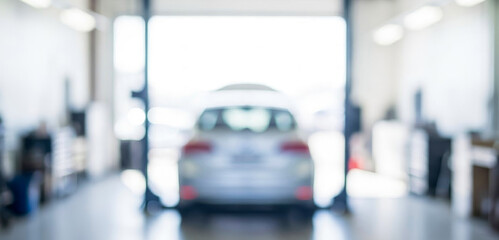 Blurred image of a car in a garage, highlighting the spacious interior. Light filters in from open doors, creating a modern atmosphere for vehicle maintenance.