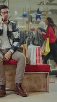 Busy mall multitasker, Casual man waits and chats on phone amidst holiday shopping chaos and festive adornments