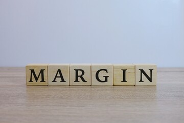 Wooden blocks spelling margin on a light brown wooden table against a white background