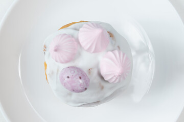 A top-down view of an Easter cake with white icing, pink meringue cookies, and a speckled candy egg, served on a white plate.