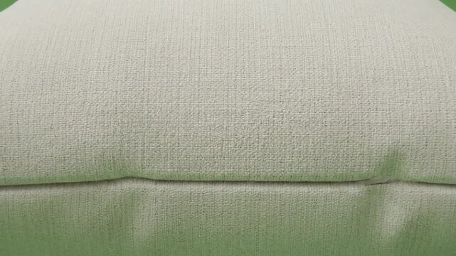 Close up of a plain off white cushion on a green background.