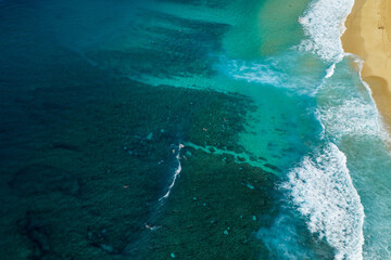 Aerial view of reef patterns and sandy patches visible through clear turquoise water at Banzai Pipeline on the North Shore of Hawaii, showing natural underwater textures.